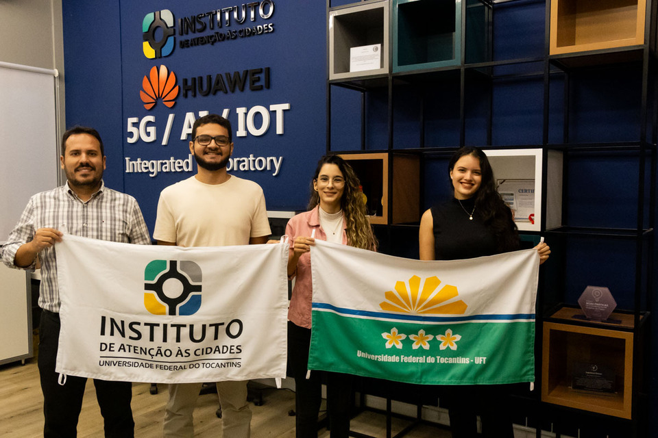 dois homens e duas mulheres seguram bandeiras da UFT e do IAC dentro de um laboraório de tecnologia da UFT