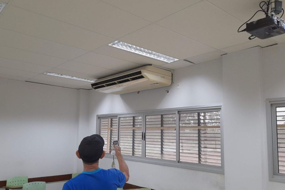Foto de um colaborador ligando um aparelho de ar-condicionado em sala de aula