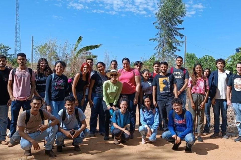Um grupo de pessoas sorrindo, algumas em pé e outras agaixadas, em ambiente aberto, com árvores ao fundo