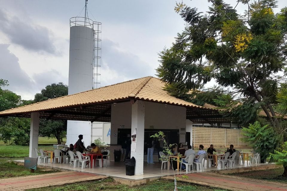 Foto externa de um dos quiosques do Câmpus onde funciona uma lanchonete, com pessoas sentadas e outras em pé, durante atendimento