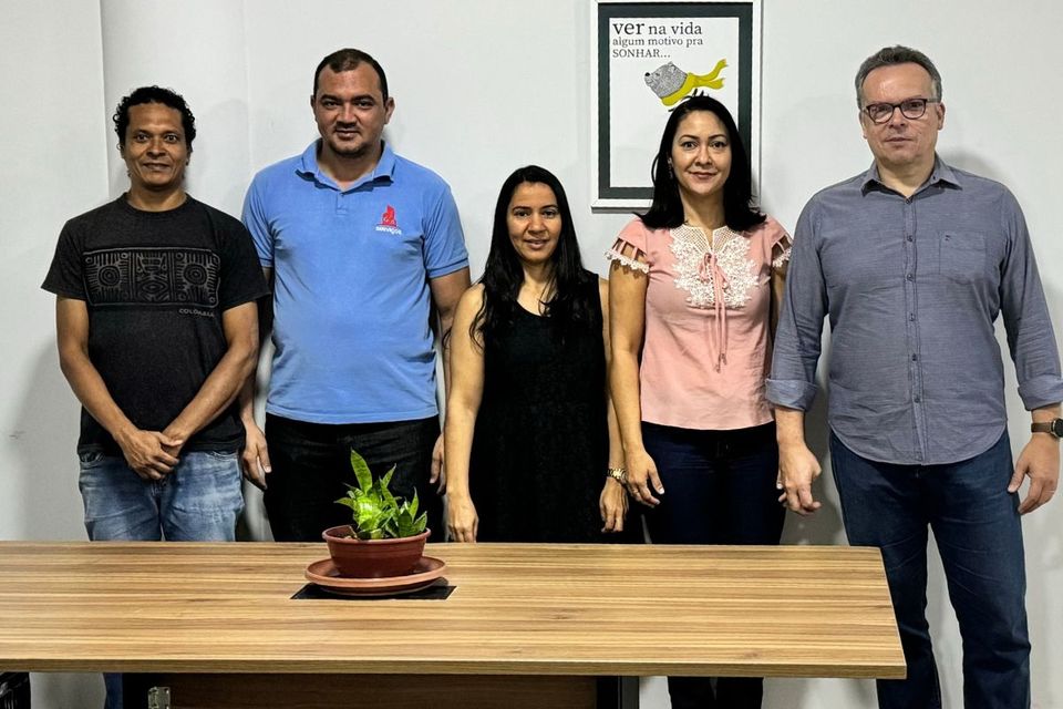 Foto com cinco pessoas em pé, ao lado de uma mesa de reuniões, membros da equipe da coordenação.