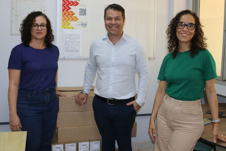 Três pessoas posam sorrindo ao lado de caixas empilhadas com novos equipamentos de informática, destinados ao Serviço de Apoio Social, Pedagógico e Psicológico do Câmpus de Palmas (UFT).