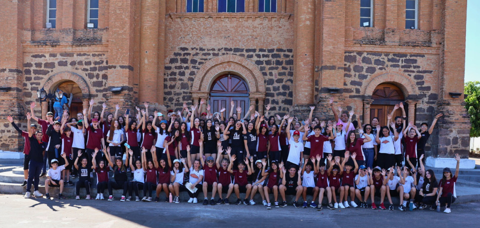 Grupo de estudantes e supervisores em frente a Catedral Nossa Senhora das Mercês com as mãos levantadas, comemorando a visita.
