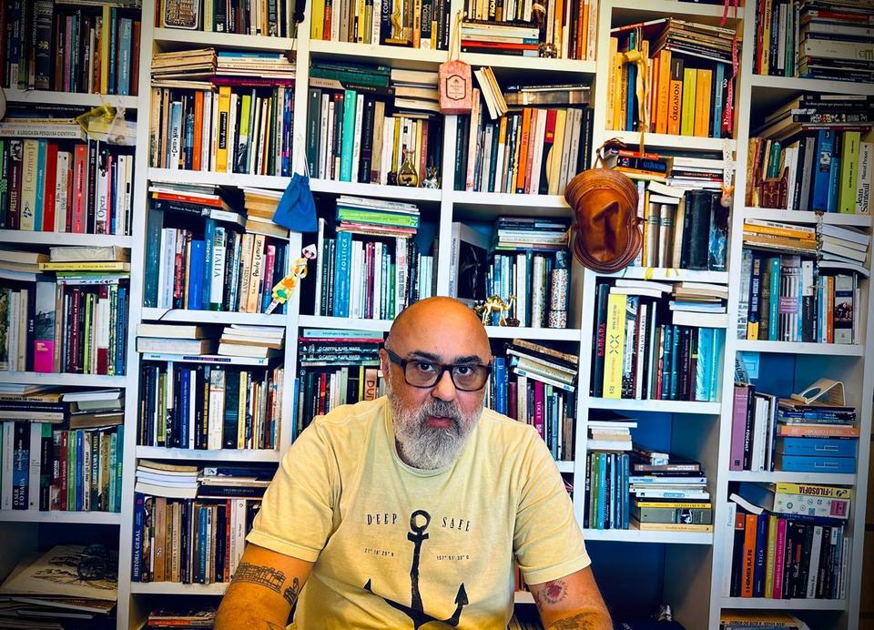 Homem com estante de livros ao fundo