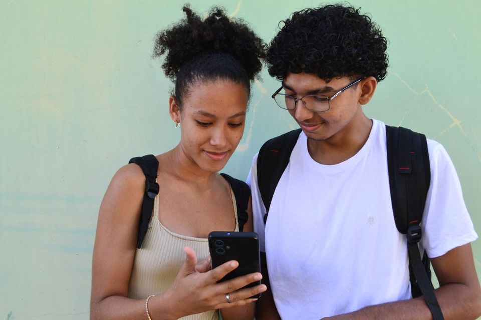 Dois jovens, uma menina e um rapaz, olham para a tela de um smartphone