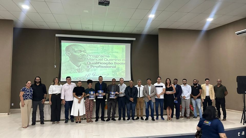 Várias pessoas que compõem o projeto estão reunidas em frente ao telão do Programa de Qualificação Manuel Querino de Qualificação Social e Profissional