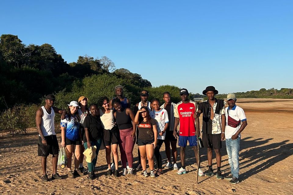 cerca de 10 pessoas reunidas em terreno arenoso com vegetação ao fundo