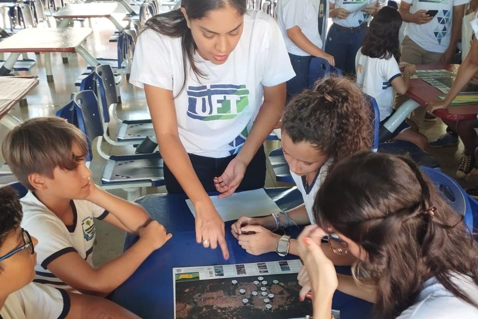 Foto com alunos de graduação em grupos com alunos do ensino fundamental, conversando com maquetes da cidade de Palmas