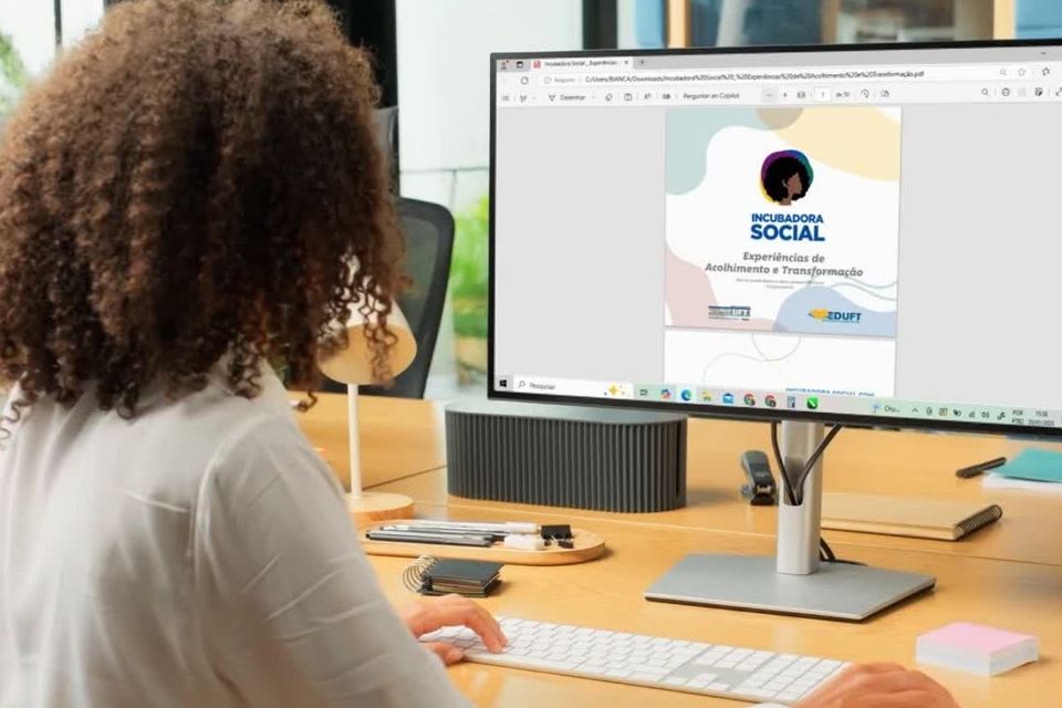 Foto de mulher de cabelos cacheados de costas, diante da tela de um computador onde se vê a capa do e-book da Incubadora Social. (Foto: Divulgação)