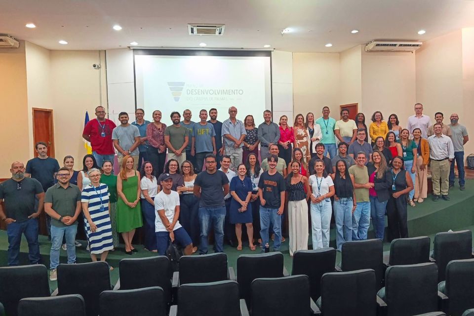 Fotografia colorida mostra um grande grupo de pessoas, entre estudantes, servidores e membros da comunidade acadêmica, reunido no auditório do Câmpus de Palmas da UFT. Os participantes estão organizados em várias fileiras, posando para a foto em frente a uma tela de projeção que exibe informações sobre o Plano de Desenvolvimento do Câmpus. À frente do grupo, aparecem cadeiras pretas do auditório.