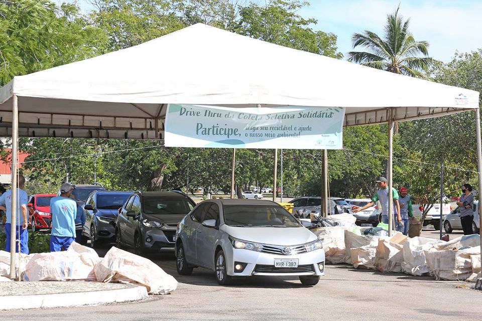 Foto de carros passando por tenda com pessoas que recolhem o material doado