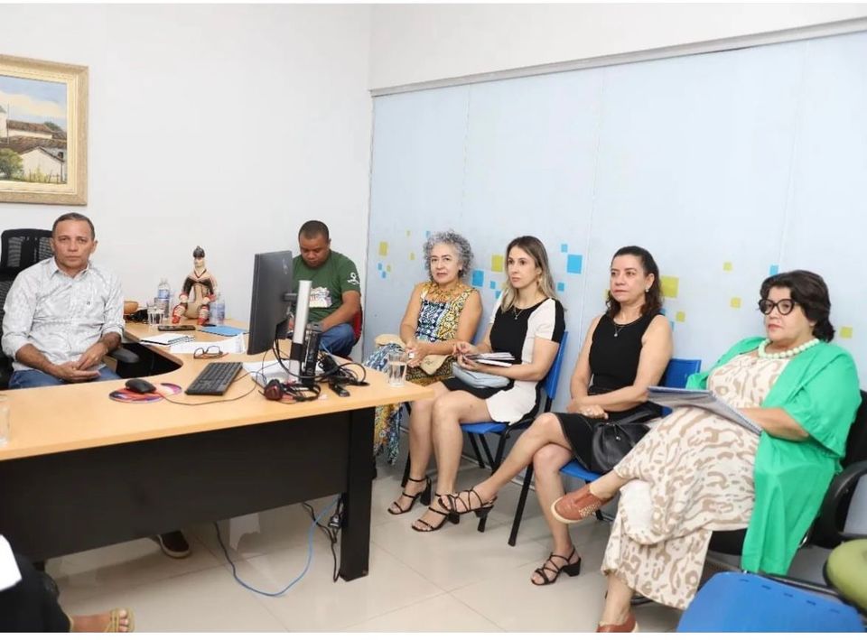 Quatro mulheres e dois homens aparecem reunidos em um escritório