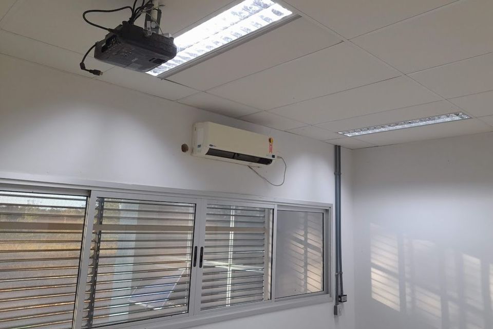 Foto da janela, teto e parede de uma sala de aula, com destaque para aparenhos datashow fixado no teto e cabos de conexão. fixados na parede